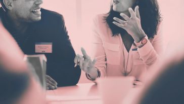 Employee engagement, two employees talking at a table during a meeting.