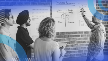 SWOT analysis image of a bald man holding a sharpie to a white paper containing a SWOT analysis. He talks to three people to his left: a sikh man, a woman with short blonde wavy hair, and a thin dark-haired man wearing glasses and a button-down shirt.