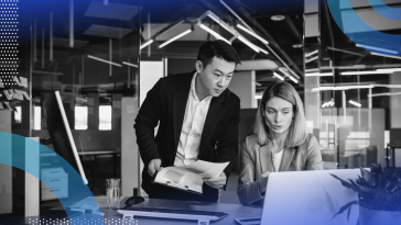 HR Operations image of a man and a woman looking at a laptop together. The woman is sitting down and pointing something out to the man. He stands next to her and leans over her shoulder.