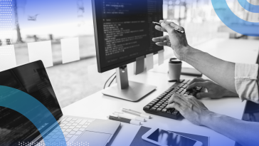 JavaScript Design Patterns image of a person sitting at a computer monitor and a laptop. He holds a pen and points to something on the desktop screen. We can see code on both screens.