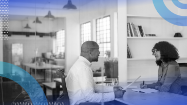 Talent assessment image of two people sitting on either side of a desk. The man on the left looks like he's explaining something to the woman on the right. She listens and takes notes.