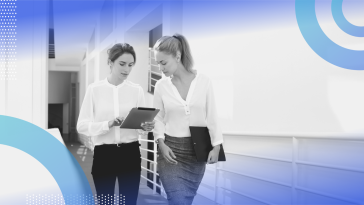 HRBP image of two women walking down a corridor. One holds an iPad and points to something on the screen, the other looks over her shoulder.