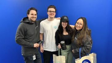 New BigTime employees pose in front of a cobalt blue wall with their Camp BigTime swag