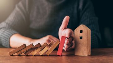 hand protecting house from falling dominoes