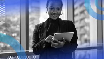 A Black business owner is standing and holding a tablet.