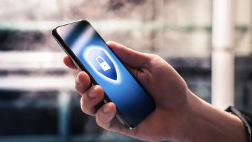 A close up of a hand holding a mobile phone with an illustration on the screen of a shield with a closed padlock in the middle.