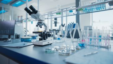 A desk is covered in test tubes, petri dishes, a microscope and other lab tools.